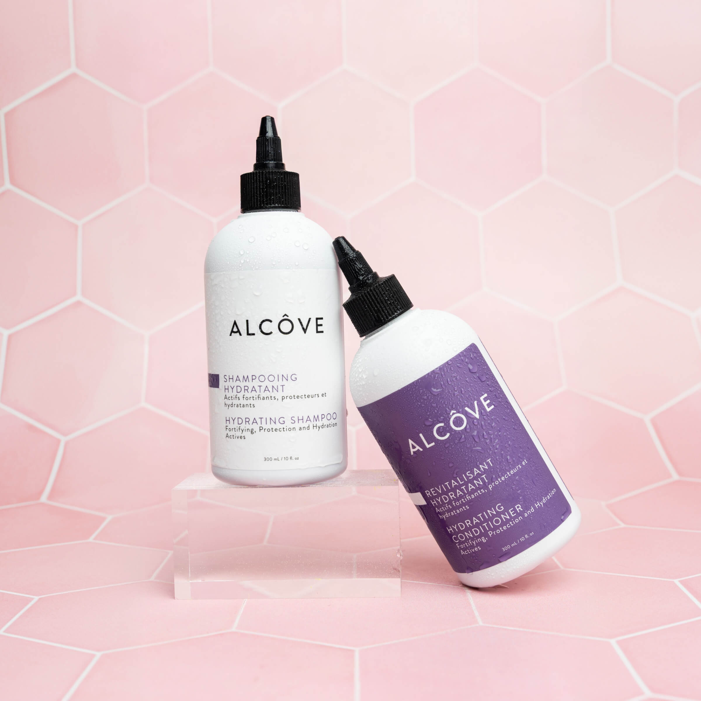 Two bottles of Alcove shampoo and conditioner on a pink geometric patterned background